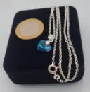 Dije de corazón 10mm de cristal azul visto de perfil con cadena de plata fina y una moneda de 100 pesos chilenos