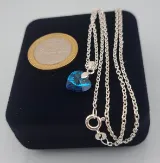 Dije de corazón 10mm de cristal azul visto de perfil con cadena de plata fina y una moneda de 100 pesos chilenos