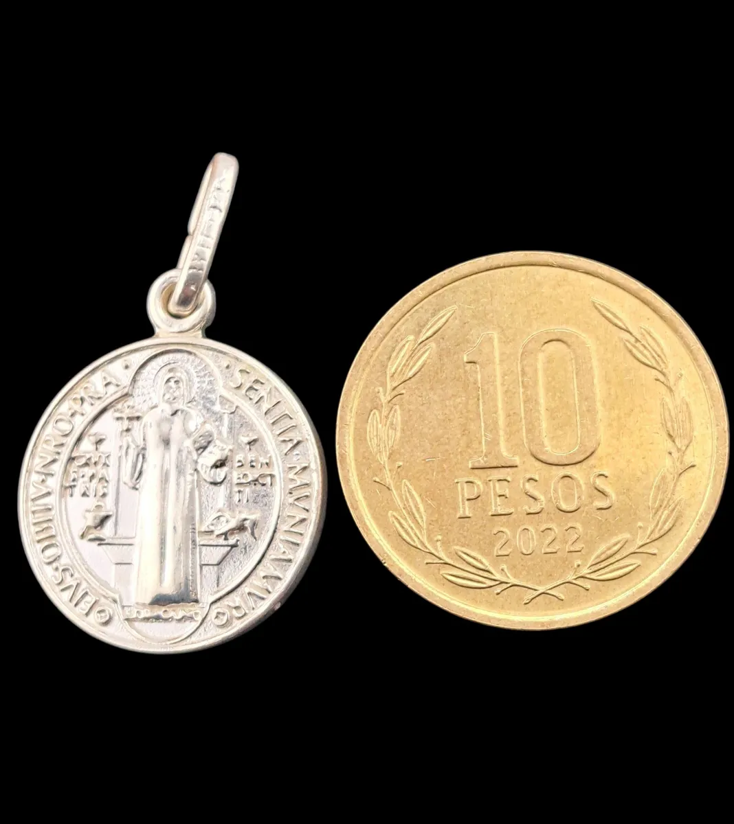 Dije San Benito de plata 925 junto a moneda de 10 pesos chilenos.